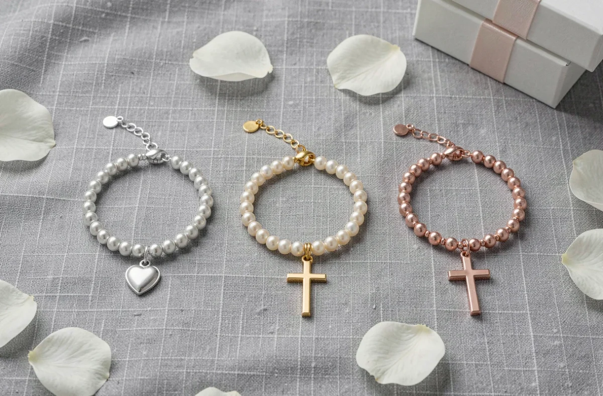 Trois bracelets de Communion en argent, or et or rose disposés sur un tissu de lin gris avec des fleurs blanches